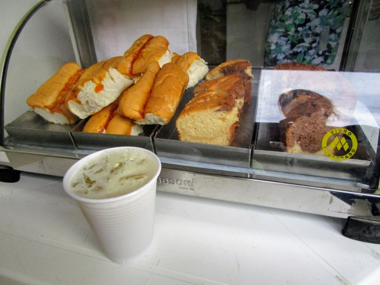 A styrofoam cup filled with caldo de cana, sugarcane juice. In front of a display of bread, as at a bakery.