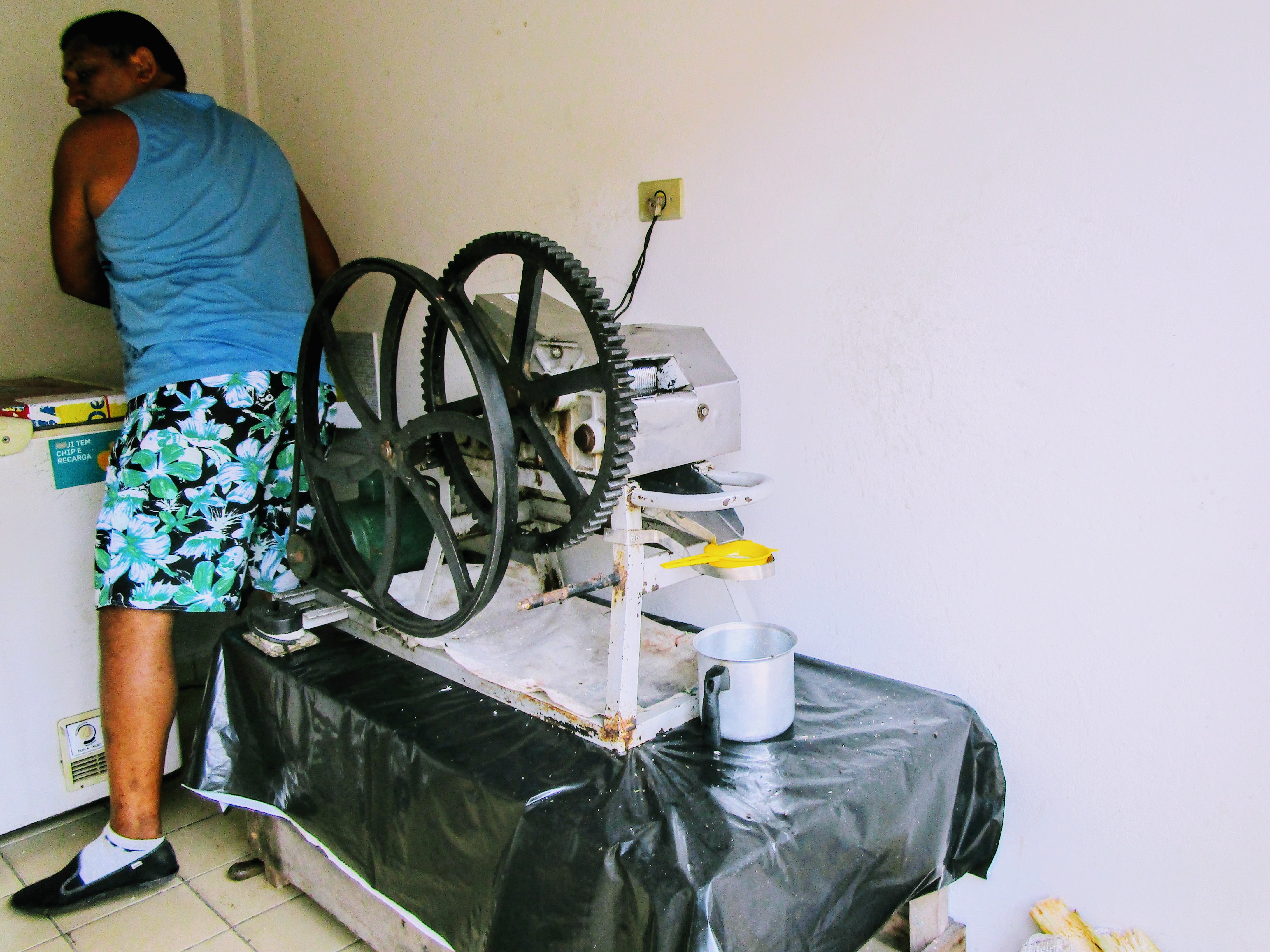 A man working with a machine that has a large wheel. The machine makes caldo de cana, sugar cane juice.