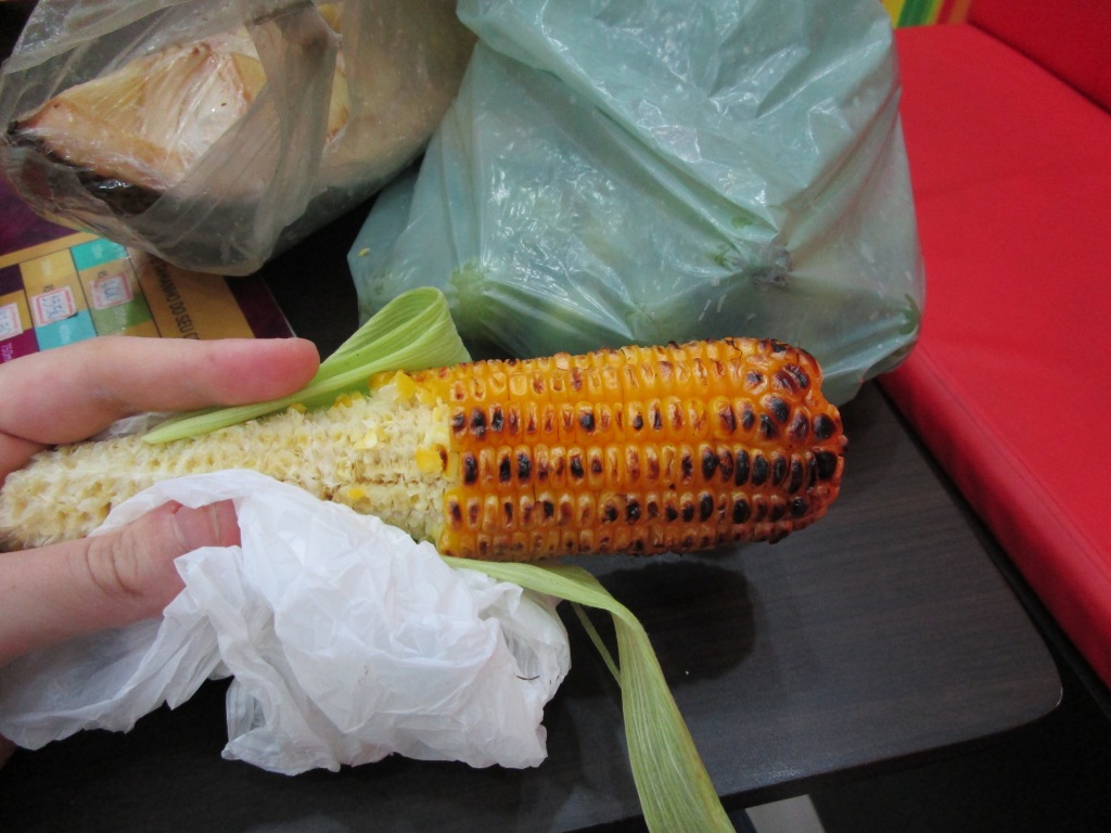 A half-eaten piece of grilled corn on the cob with many blackened kernels.